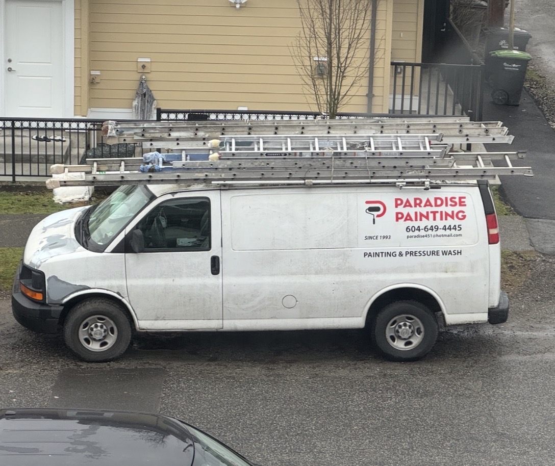 A Paradise Painting van carrying ladders, with the company logo and Since 1993 lettering, parked outside a home.